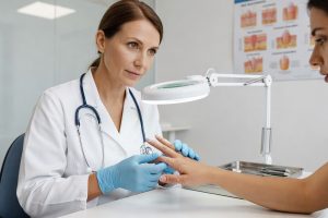 Dermatoloog wijst witte vlekken aan op nagels van patiënt tijdens consult in kliniek