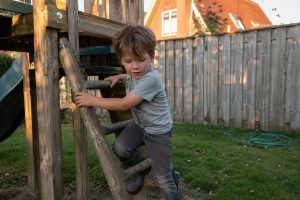 Kind klimt spelenderwijs op een houten speeltoestel in de tuin
