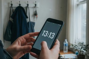 Handen met smartphone die 13:13 toont in een gang met daglicht