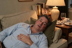 Man op sofa na maaltijd met hand op borst in woonkamer