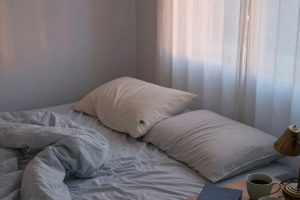 Onopgemaakt bed in ochtendlicht met twee koffiekopjes op het nachtkastje